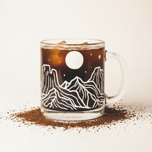 Load image into Gallery viewer, Clear mug with mountain and moon design held by a person wearing a white sweater.